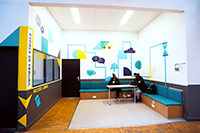 Photographie du tiers-lieu du bâtiment B, espace de détente dans lequel ont été amménagées des banquettes et dont les murs ont été décorés de fresques.